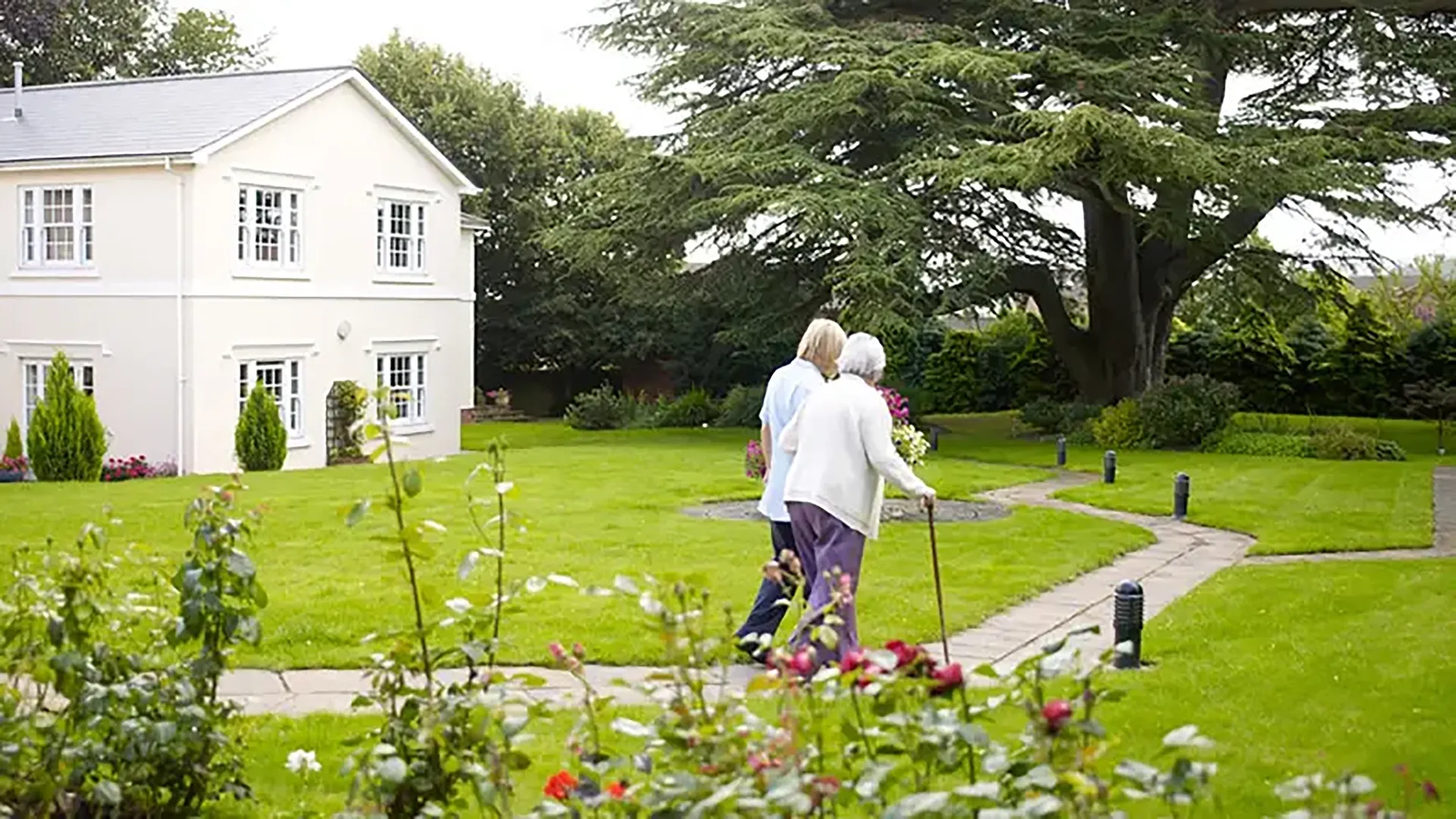 Carer walking with elderly person in pretty care home garden