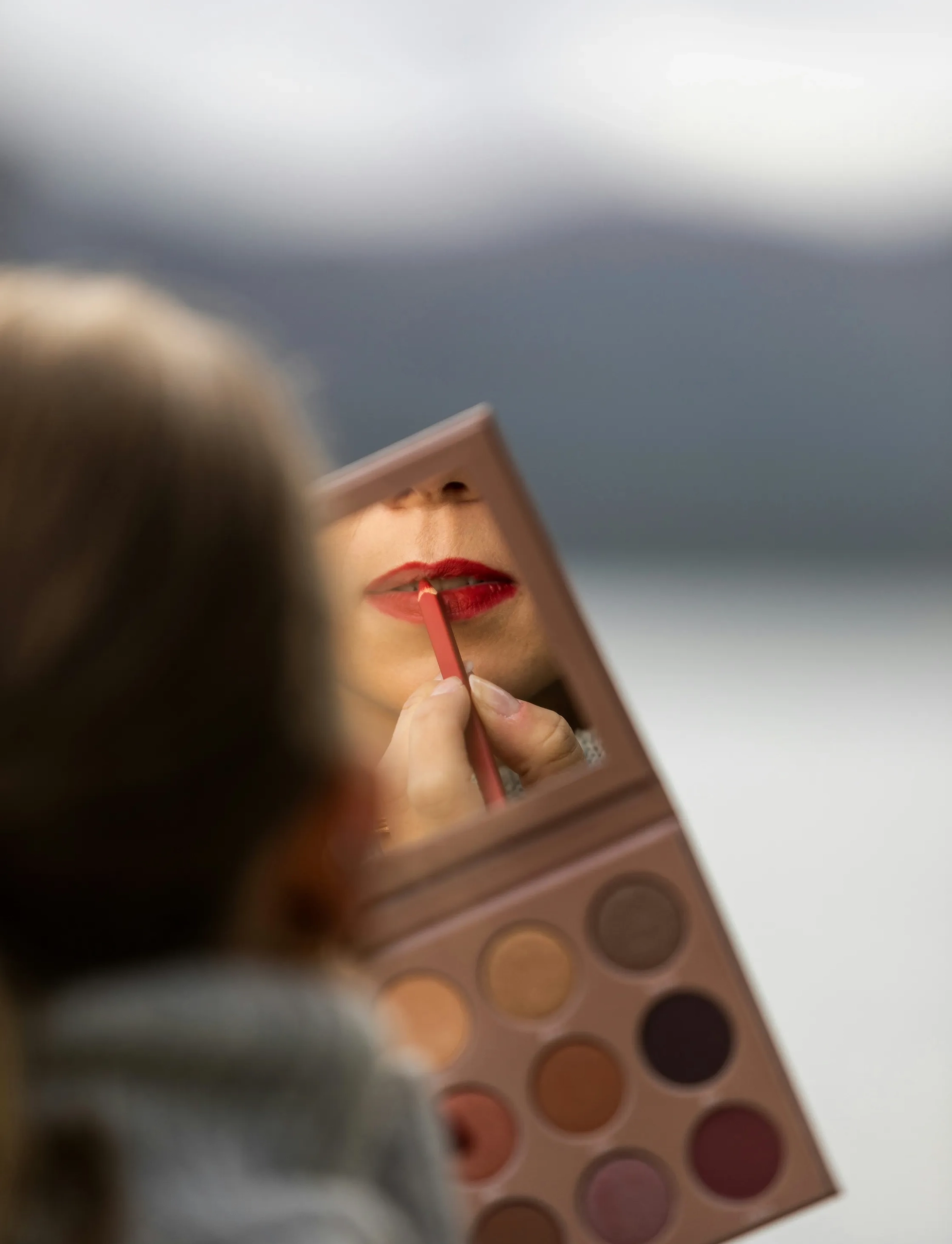 Close-up of person looking in a mirror applying lipstick